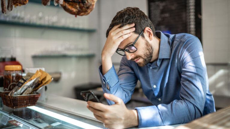 Właściciel firmy patrzy w telefon i czeka na zapytania ze strony internetowej
